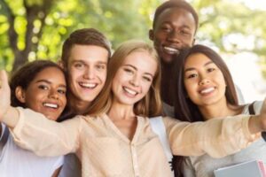 Five teenagers smiling for a group selfie.