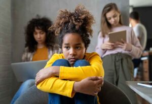 A sad Black girl hugging her knees and looking lost in thoughts. 