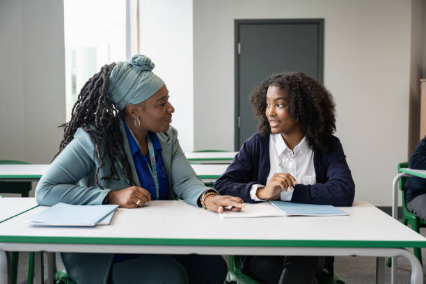 How to choose the right tutor for your child. A supportive female tutor in her early 50s sitting at a desk with a teenage schoolgirl while discussing an assignment.